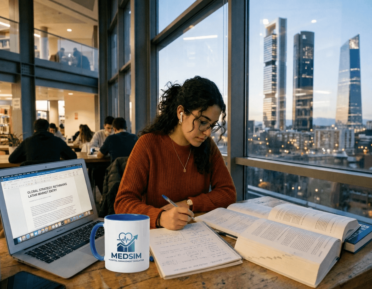 Estudiante con suéter naranja estudia con laptop y libros frente a ventanal con rascacielos.